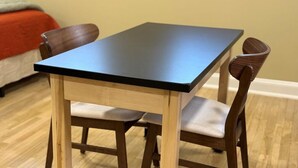 A small dining table with a black top and wooden legs, accompanied by two wooden chairs with cushioned seats.