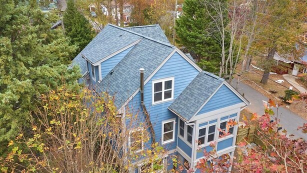 A blue house with a steep roof, surrounded by trees and a small garden.