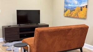 A living room with a dark wooden entertainment center, a flat-screen TV, a brown sofa, and a painting of autumn foliage on the wall.