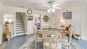 A dining area with a wooden table, white chairs, a ship's wheel, and nautical-themed decor. - Galveston Bay Retreat: Historic La Porte Home! (La Porte)