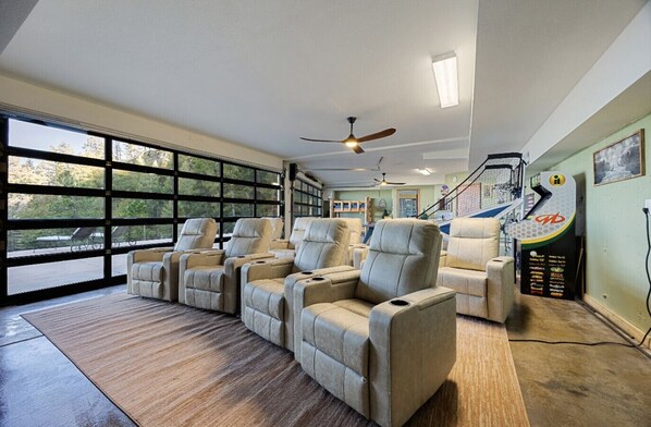 A spacious room with large windows, a ceiling fan, and a seating area with multiple recliners.