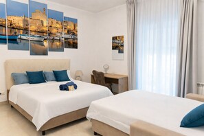 A hotel room with two beds, a desk, a chair, and artwork on the walls.