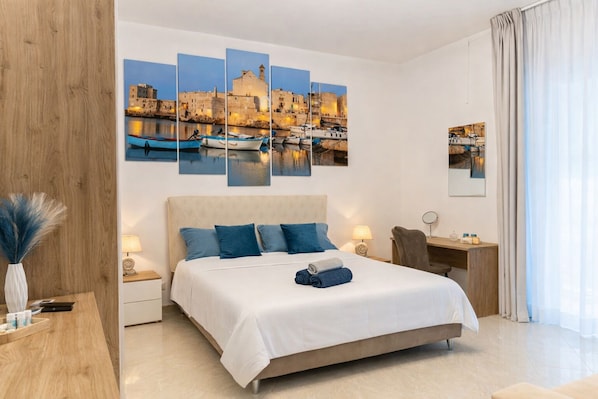 A hotel room with a large bed, a desk, a chair, a nightstand, and a wall with a cityscape painting.