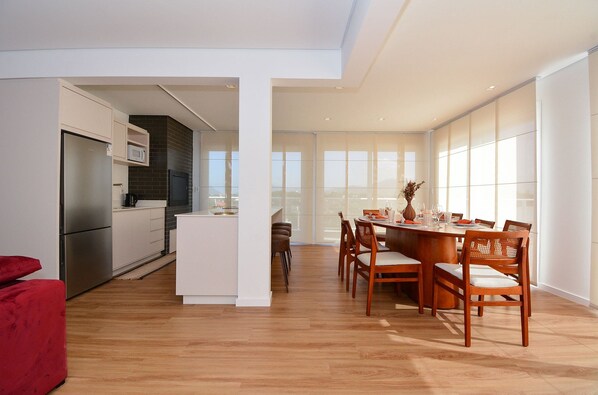 A modern kitchen with a built-in microwave, a dining area with wooden chairs and a table, and large windows providing natural light. - Cobertura SunClub-300 mtrs da Praia  (Florianopolis)
