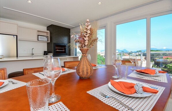A dining area with a large table set for six, a modern kitchen in the background, and a view of the city through large windows. - Cobertura SunClub-300 mtrs da Praia  (Florianopolis)