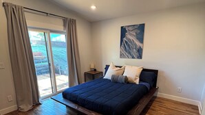 Ein Schlafzimmer mit einem großen Bett, Holzboden, einer Schiebetür zu einem Balkon und einem Gemälde an der Wand.
