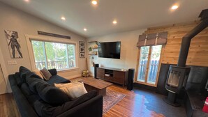 Ein Wohnzimmer mit schwarzem Sofa, Holzboden, Wandfernseher und Kaminofen.