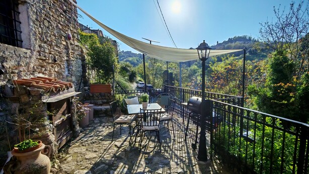 Una terraza con suelo de piedra, mobiliario exterior y vistas a un paisaje montañoso.