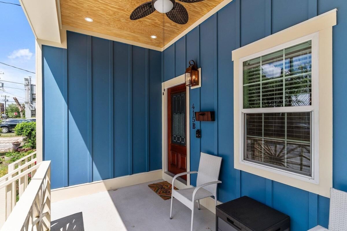 A blue exterior with a white door, a window with blinds, a white chair, and a ceiling fan.