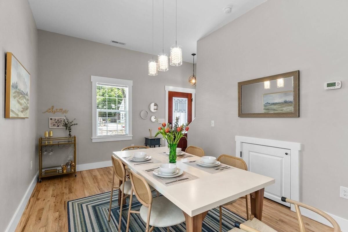 A dining area with a table set for four, a vase with flowers, a fireplace, and a window with blinds.
