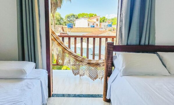 A hotel room with two beds, a wooden headboard, and a view of a balcony with a hammock. - POUSADA SOL DE VERAO - Cumuruxatiba (Cumuruxatiba)