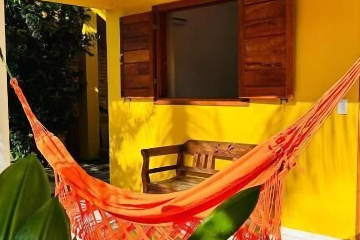 A yellow building with a wooden balcony, a hammock, and a bench.