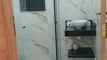 Ein Badezimmer mit Duschkabine aus Glas, einem weißen Waschbecken mit Schüssel und einer Toilette.