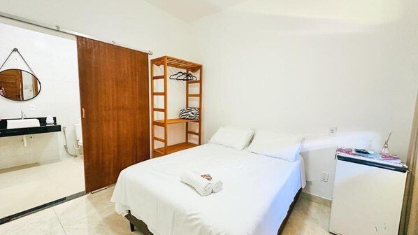 A hotel room with a bed, a wooden wardrobe, a mirror, a small table, and a refrigerator. - POUSADA SOL DE VERAO - Cumuruxatiba (Cumuruxatiba)