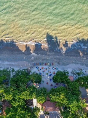 An aerial view of a beach with umbrellas and lounge chairs arranged in a semi-circle, surrounded by lush greenery and a clear view of the ocean. - POUSADA SOL DE VERAO - Cumuruxatiba (Cumuruxatiba)