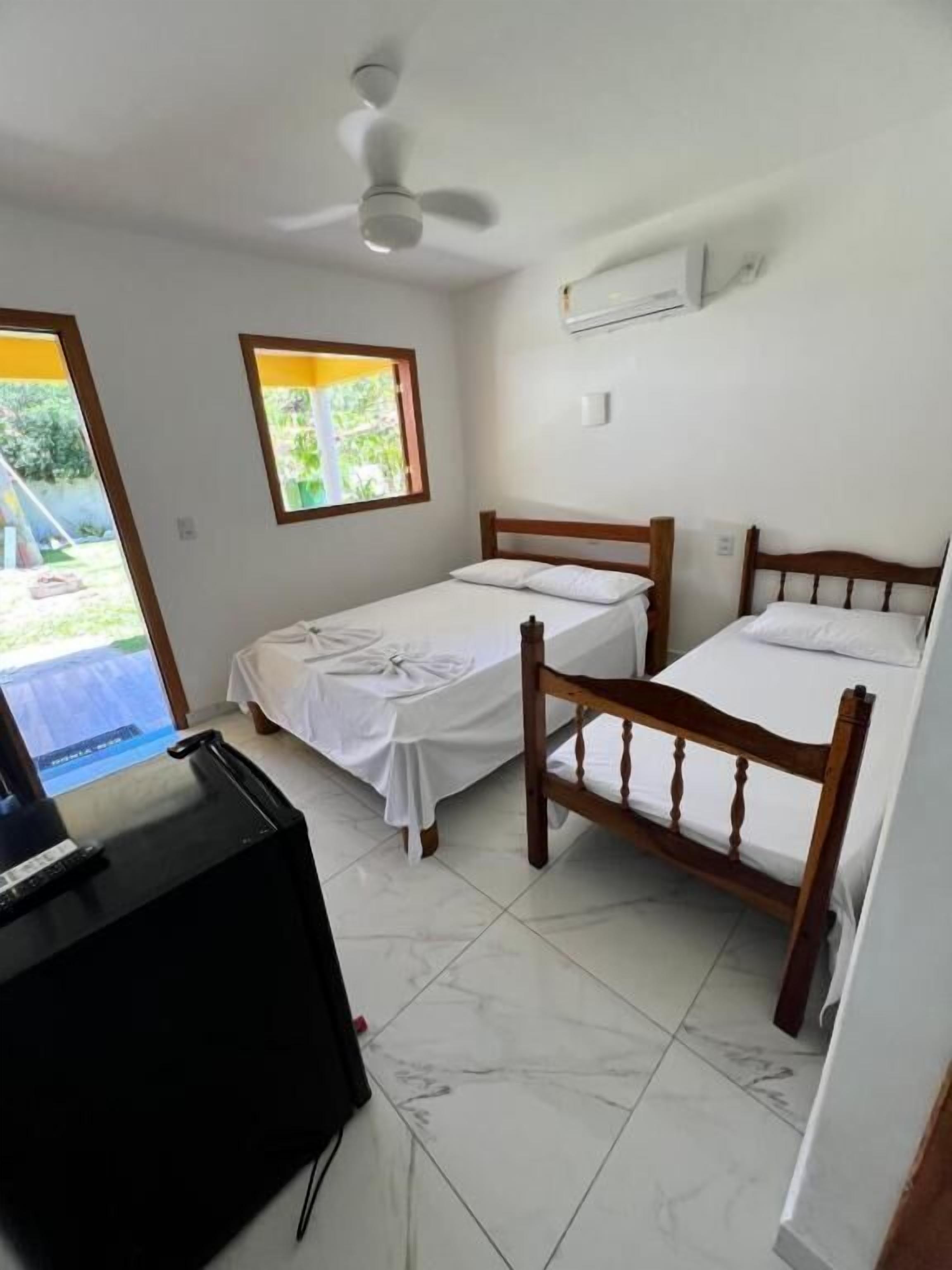 A room with two wooden beds, a ceiling fan, a window with a view of greenery, and a desk with a computer.
