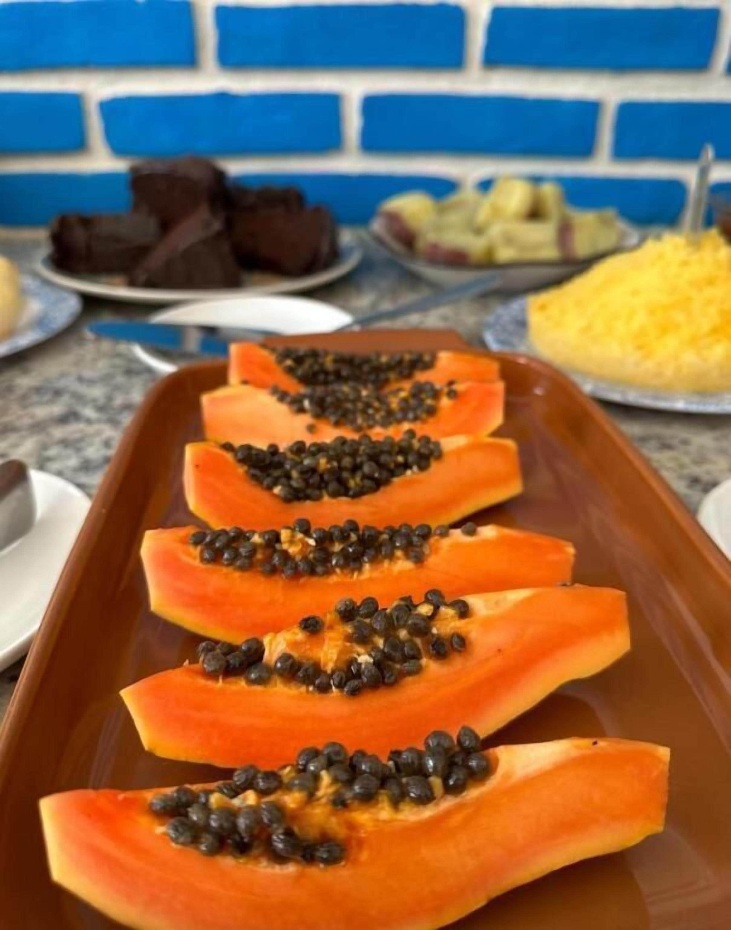 Rebanadas de papaya dispuestas en una bandeja, con un muro de ladrillo azul al fondo.