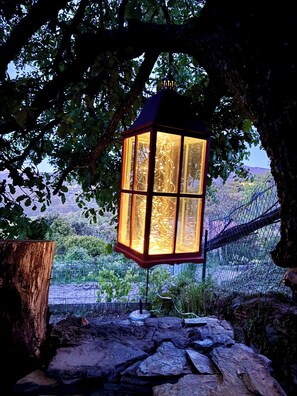 Un farol colgando bajo un árbol, rodeado por un sendero de piedra y una cerca de alambre.