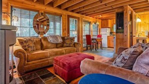 L’intérieur chaleureux d’un chalet avec un plafond en bois, un canapé, un pouf rouge et un coin repas.