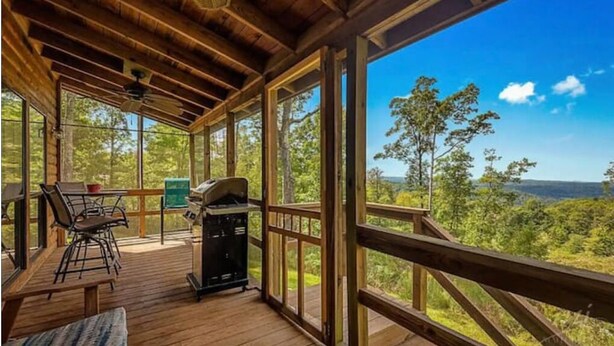 Une terrasse extérieure couverte, équipée d’un barbecue, d’un espace salon et de grandes fenêtres offrant une vue sur la forêt environnante.