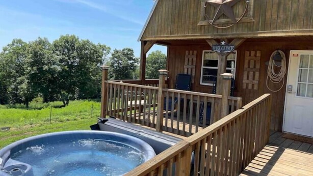 A wooden cabin with a hot tub on the deck, a welcome sign, and a star logo. - Buffalo River Cowboy Cabin Getaway and HOT TUB! (Compton)