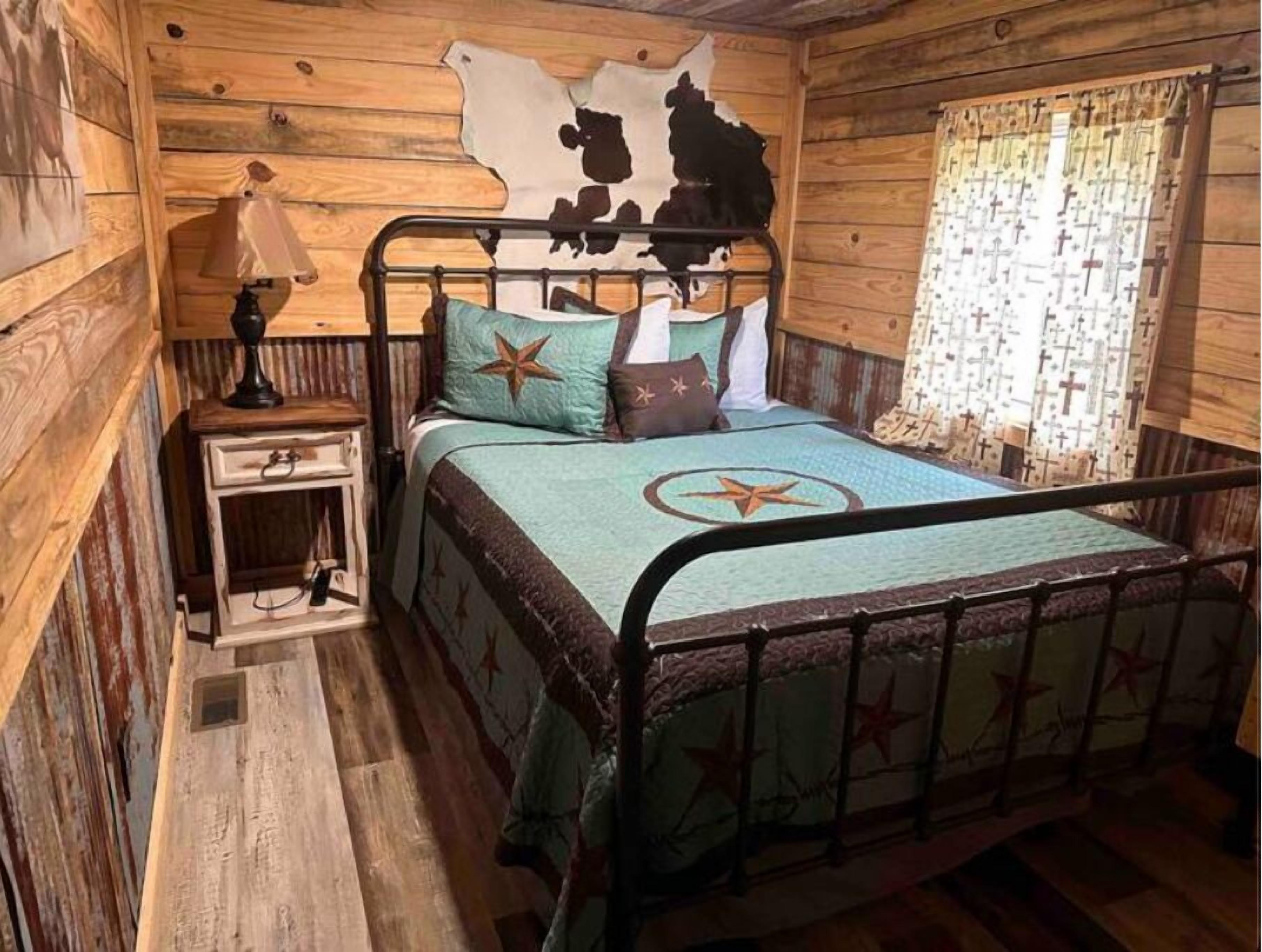 A rustic wooden room with a bed, a nightstand, and a wall with a cowhide pattern.