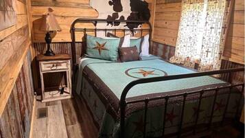 A rustic wooden room with a bed, a nightstand, and a wall with a cowhide pattern.