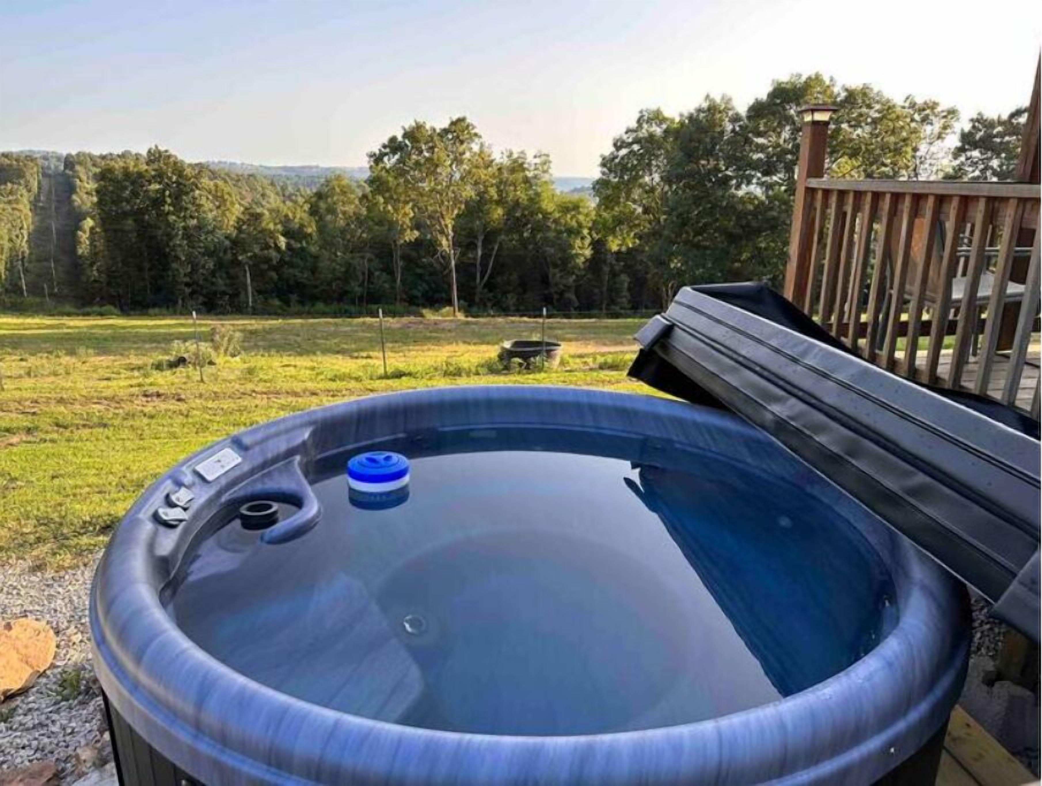 Un jacuzzi en una terraza al aire libre con vistas a un campo cubierto de césped y árboles.