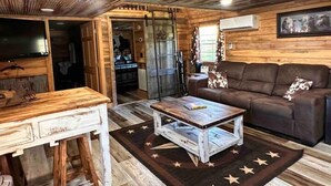 A rustic cabin interior with a wooden ceiling, a brown leather sofa, a wooden coffee table, and a television on a wooden stand. - Buffalo River Cowboy Cabin Getaway and HOT TUB! (Compton)
