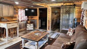 A rustic cabin interior with a wooden dining table, a sofa, and a television. - Buffalo River Cowboy Cabin Getaway and HOT TUB! (Compton)