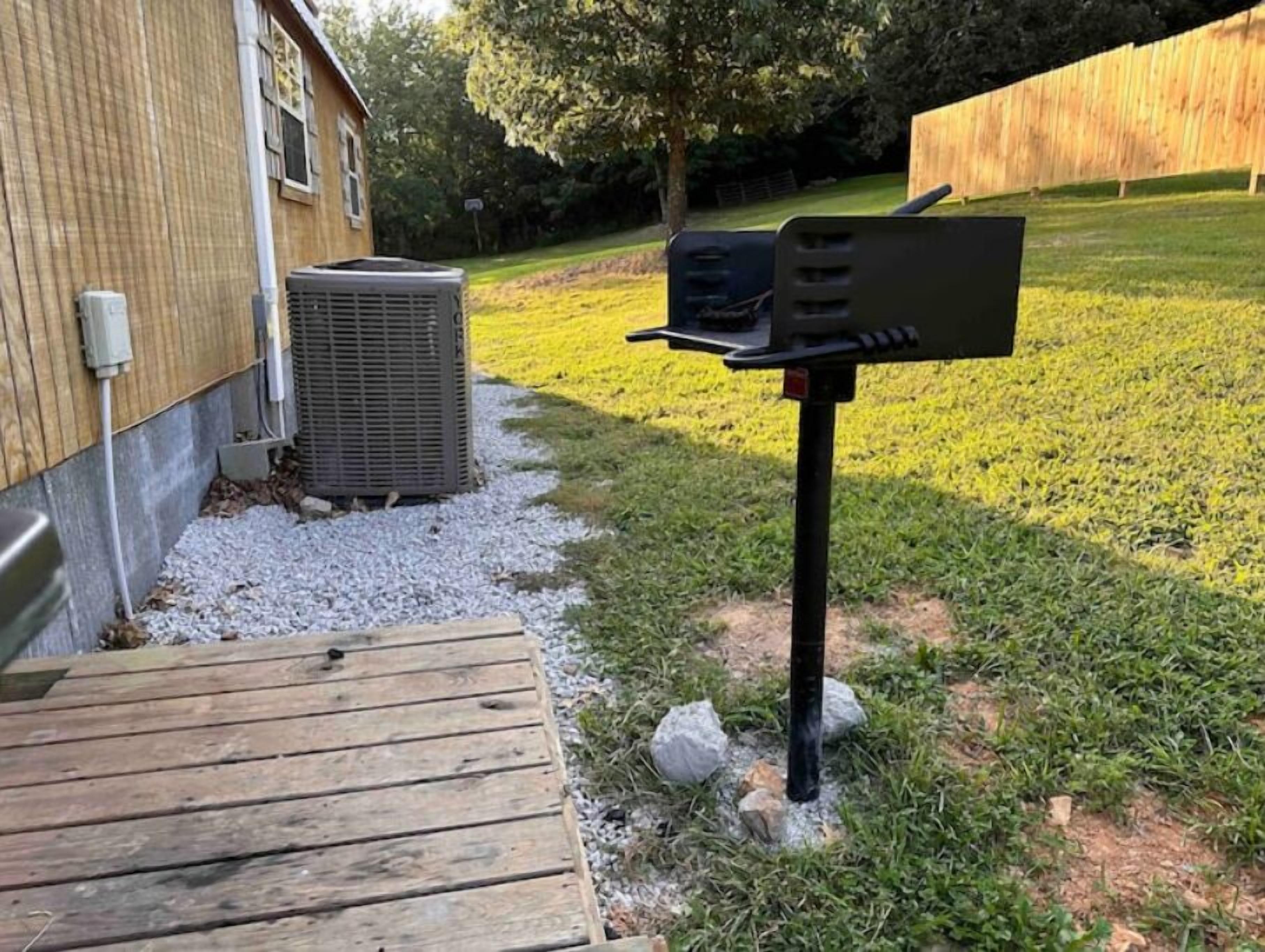 A wooden deck leading to a building with an air conditioning unit and a mailbox.