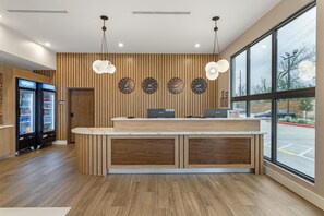Un área de recepción con un mostrador de madera, dos refrigeradores y relojes que muestran nombres de diferentes ciudades.
