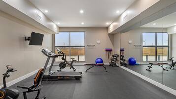 Un gimnasio con equipo de ejercicio, ventanas amplias y un espejo que refleja el espacio.