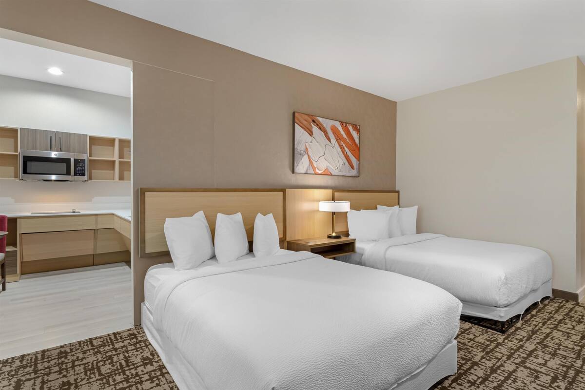 A hotel room with two beds, a desk with a microwave, a lamp, and a painting on the wall.