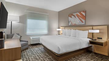Une chambre d’hôtel moderne avec un grand lit, des tables de chevet avec des lampes, un téléviseur à écran plat, un canapé gris et un tapis à motifs.