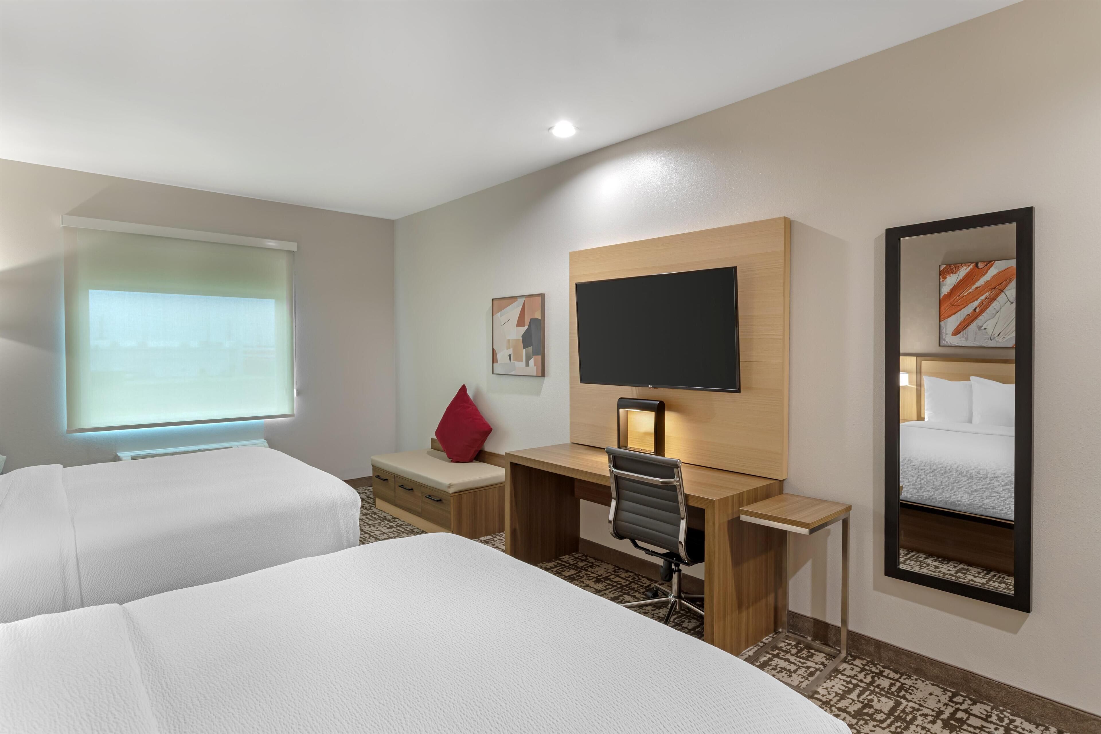 Habitación de hotel con dos camas, un escritorio, una silla, un televisor y un espejo.