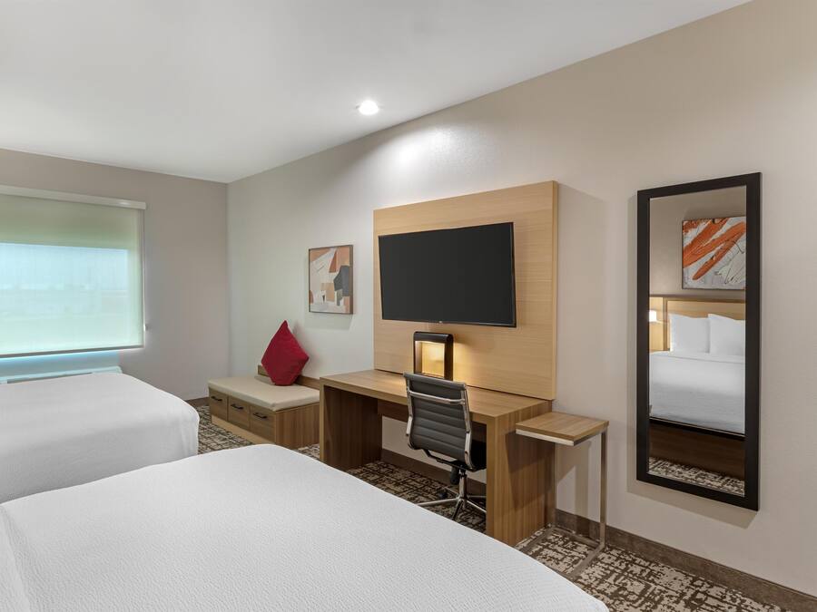 A hotel room with two beds, a desk, a chair, a TV, and a mirror.