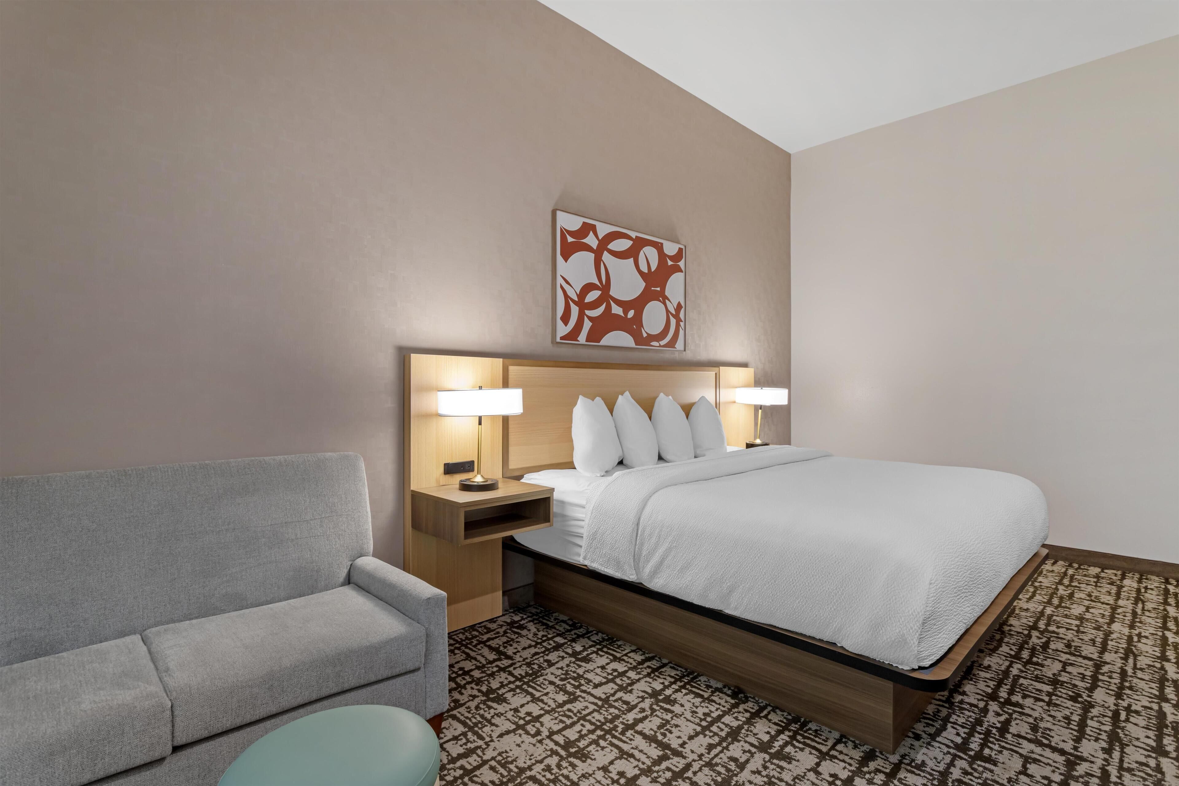 A hotel room with a bed, a sofa, a patterned rug, and a wall art piece.