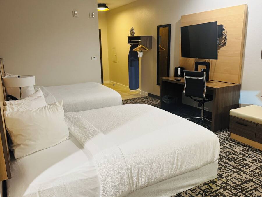 A hotel room with two single beds, a desk with a chair, a television, and a mirror.