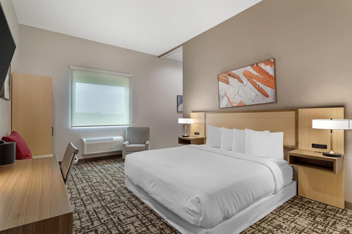 Hotelkamer met een groot bed, een bureau, een stoel, een raam en een kunstwerk aan de muur.