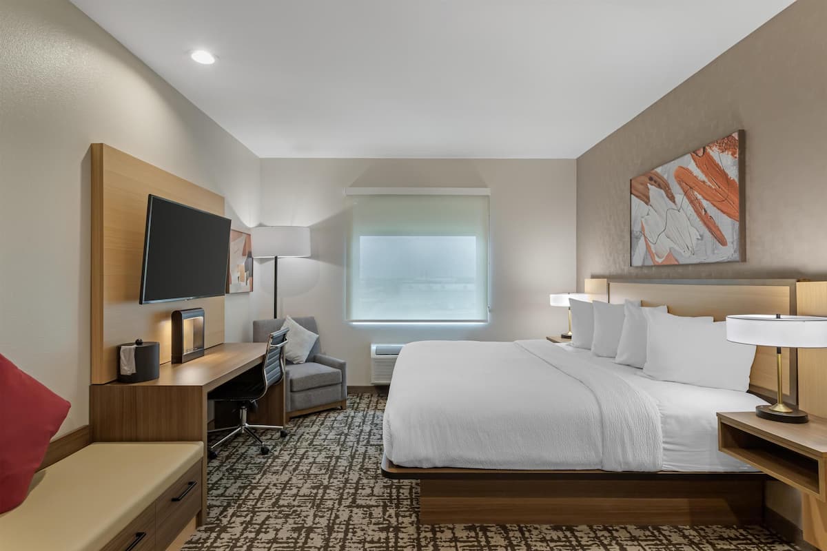 A hotel room with a bed, desk, chair, TV, and artwork on the wall.