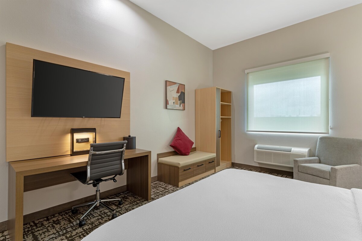 Een hotelkamer met een bed, een bureau met stoel, een televisie, een kledingkast en een raam.