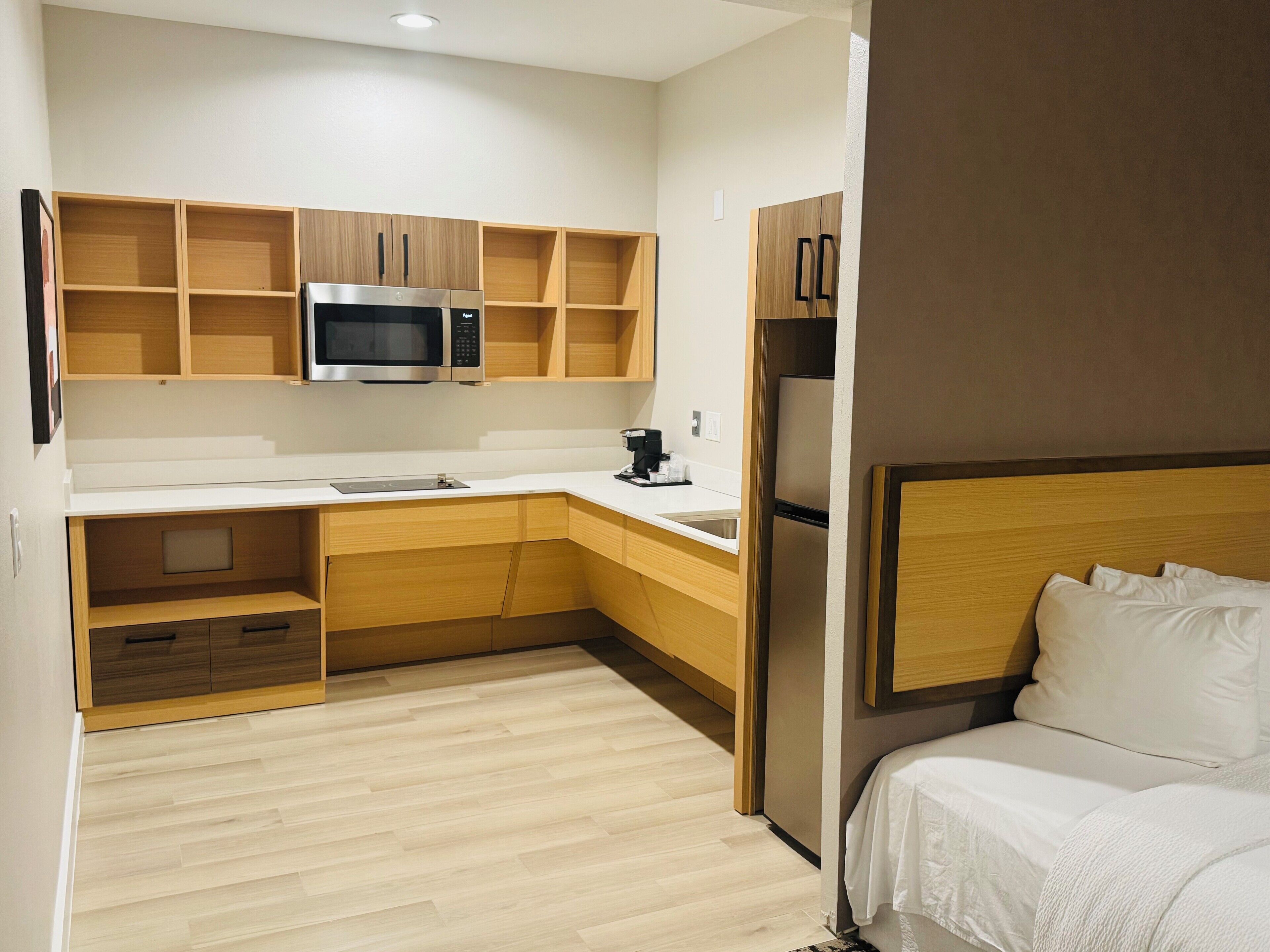 Una habitación de hotel compacta con kitchenette, una cama y un cabecero de madera.