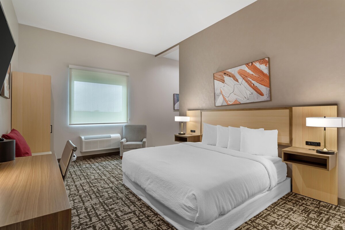 Hotelkamer met een groot bed, een bureau, een stoel, een raam en een kunstwerk aan de muur.