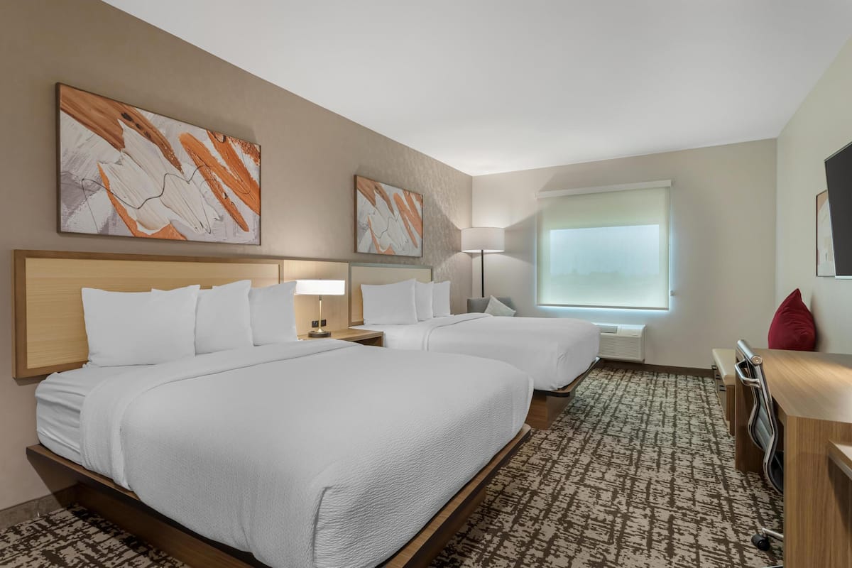 Een hotelkamer met twee bedden, een bureau, een stoel, een lamp en kunstwerken aan de muur.