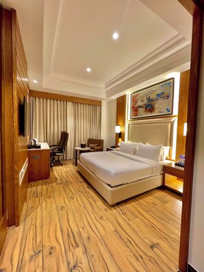 A hotel room with a large bed, a desk with a chair, a small table, and a painting on the wall.