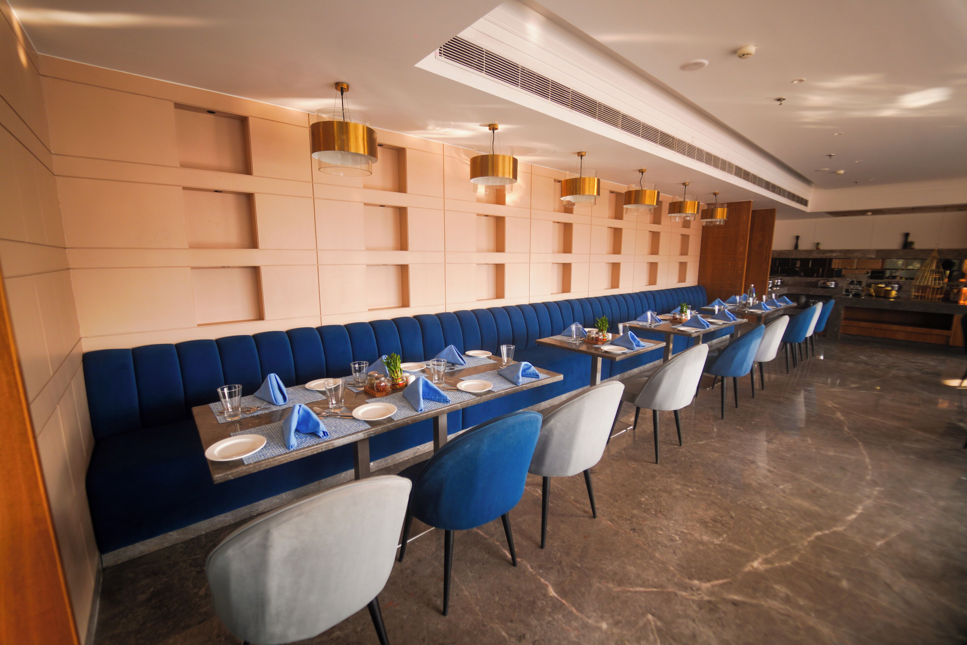 A modern restaurant with a long counter, blue upholstered booths, and a variety of seating options including chairs and tables.