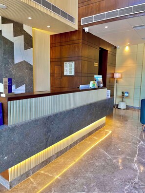 A modern reception desk with a marble floor, a wooden panel wall, and a digital screen displaying information.