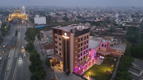 A multi-story hotel with a prominent entrance, a parking area, and a landscaped courtyard.
