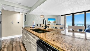 A modern kitchen with granite countertops, a built-in sink, and a dining area with a view of the ocean. - Edgewater Tower 2-608 (Panama City Beach)